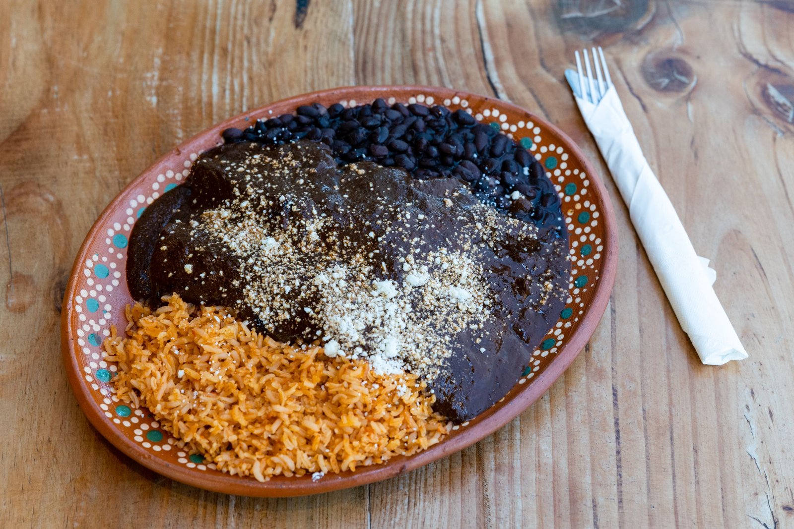 A colorful plate of Mexican mole with rice and beans on a rustic wooden table.
