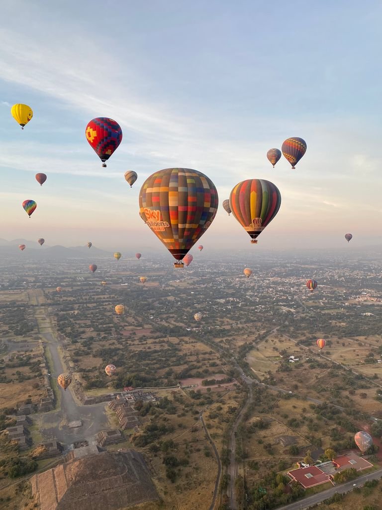 Colorful hot air balloons soar above San Juan Teotihuacán, Mexico, offering a breathtaking aerial view.