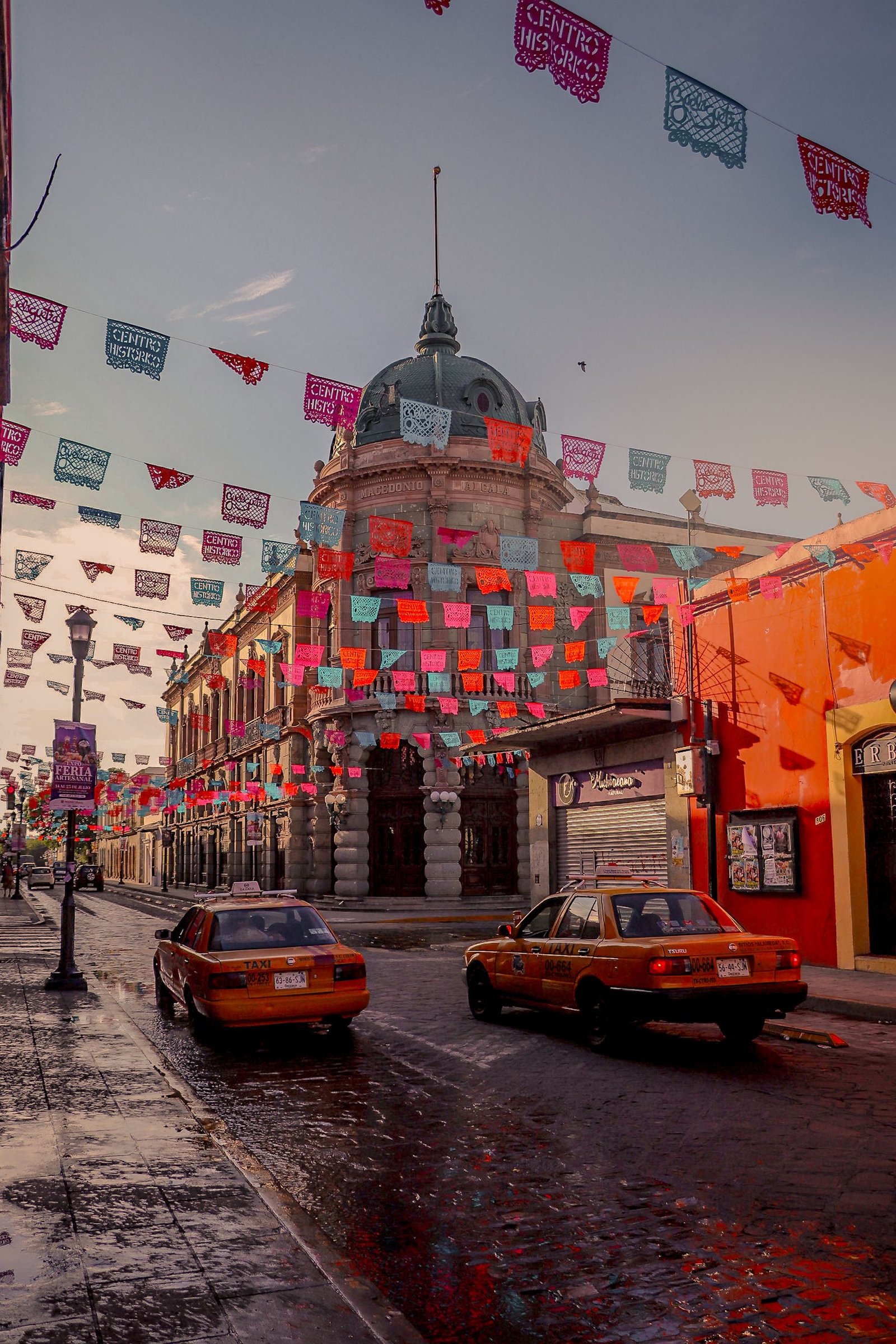 Colorful papel picado decorates the streets of Oaxaca, Mexico, with taxis passing by.