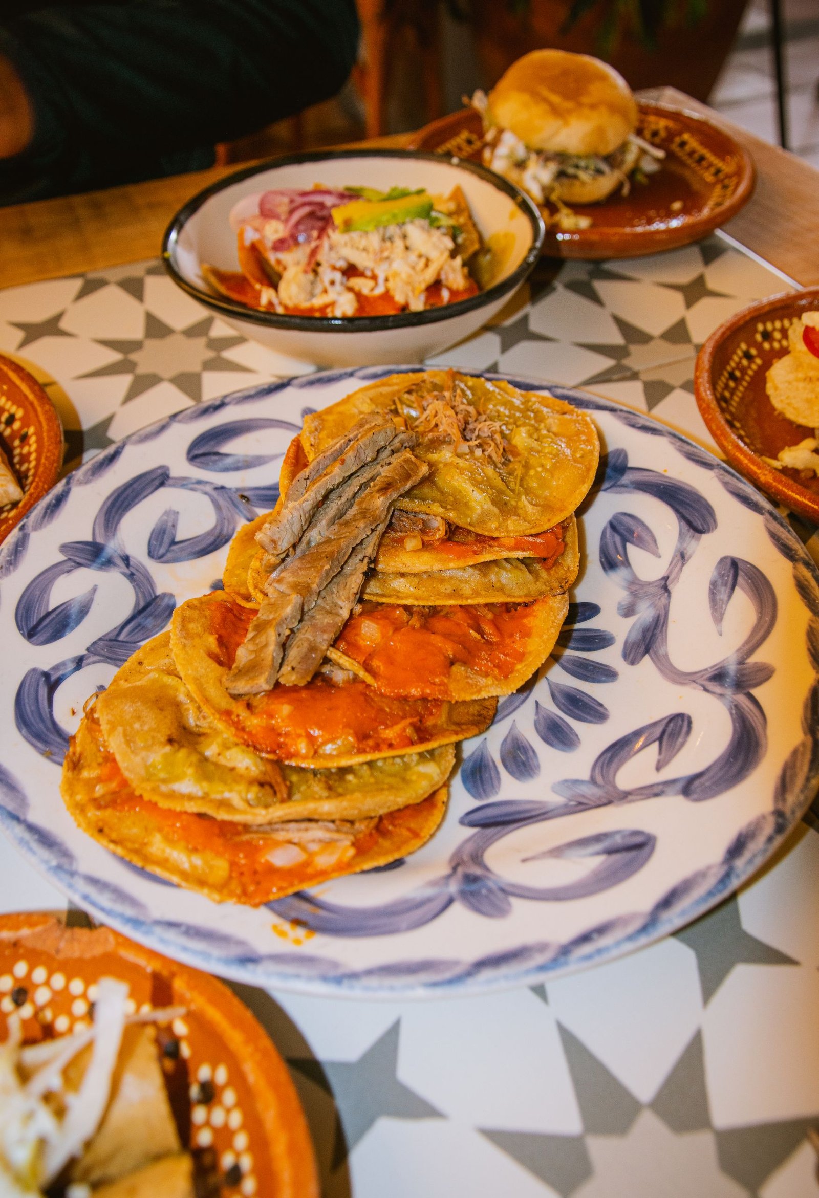 Delicious Tlayuda dish with toppings on a decorative plate, served in a vibrant Mexican setting.