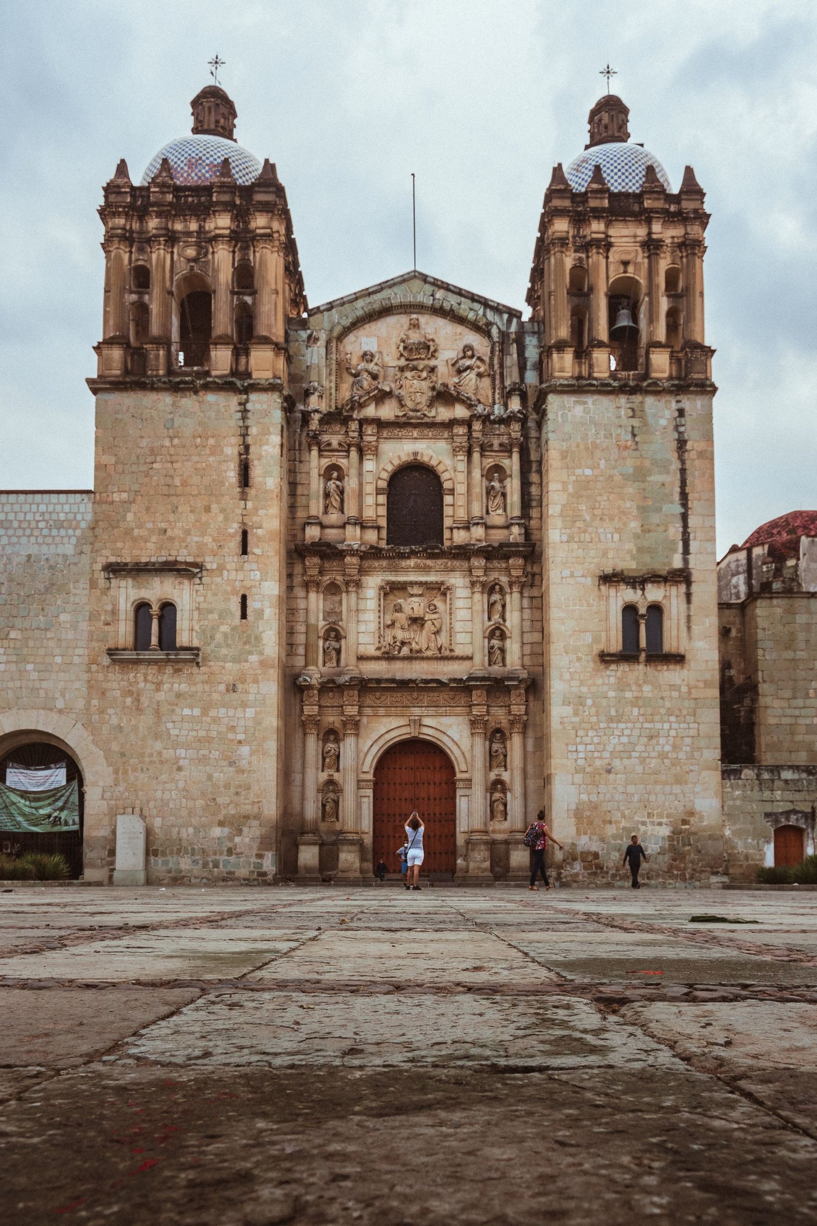Detailed view of a historic Baroque church facade in Oaxaca, Mexico under a cloudy sky.