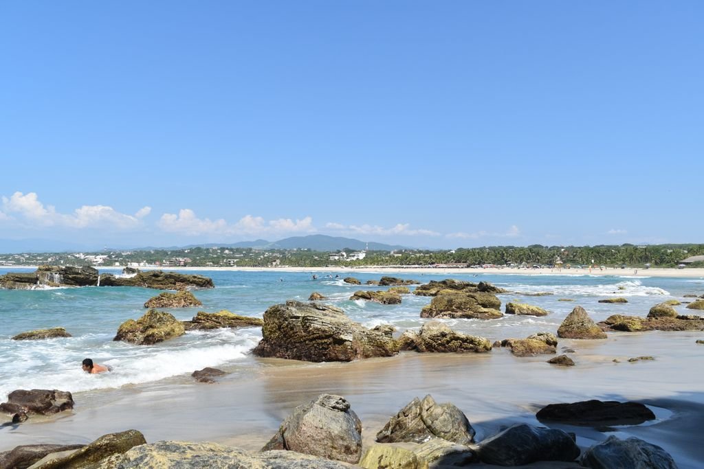 Explore the stunning beaches of Puerto Escondido, Oaxaca, Mexico with clear blue skies and rocky shores.