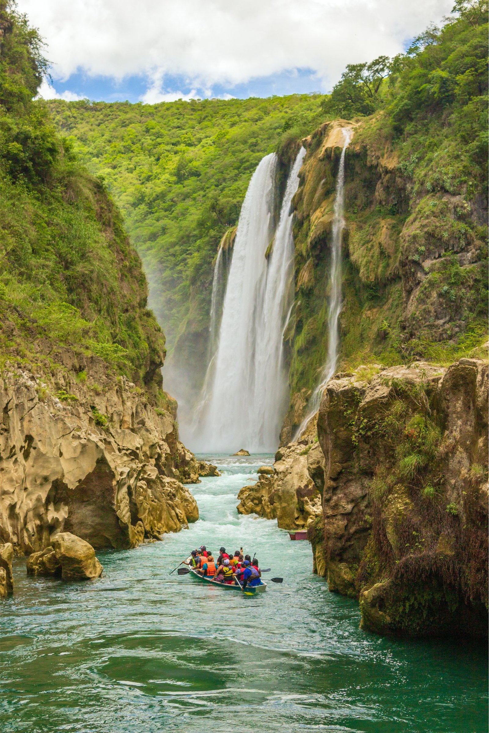 Kayakers navigate through the stunning Tamasopo Falls surrounded by lush greenery.