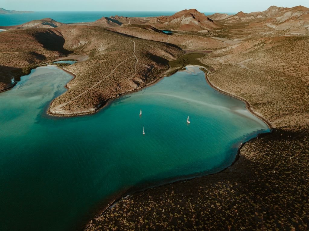 Stunning aerial shot of Pichilinque Bay, BCS, Mexico with sailboats and vibrant blue water surrounded by rugged terrain.