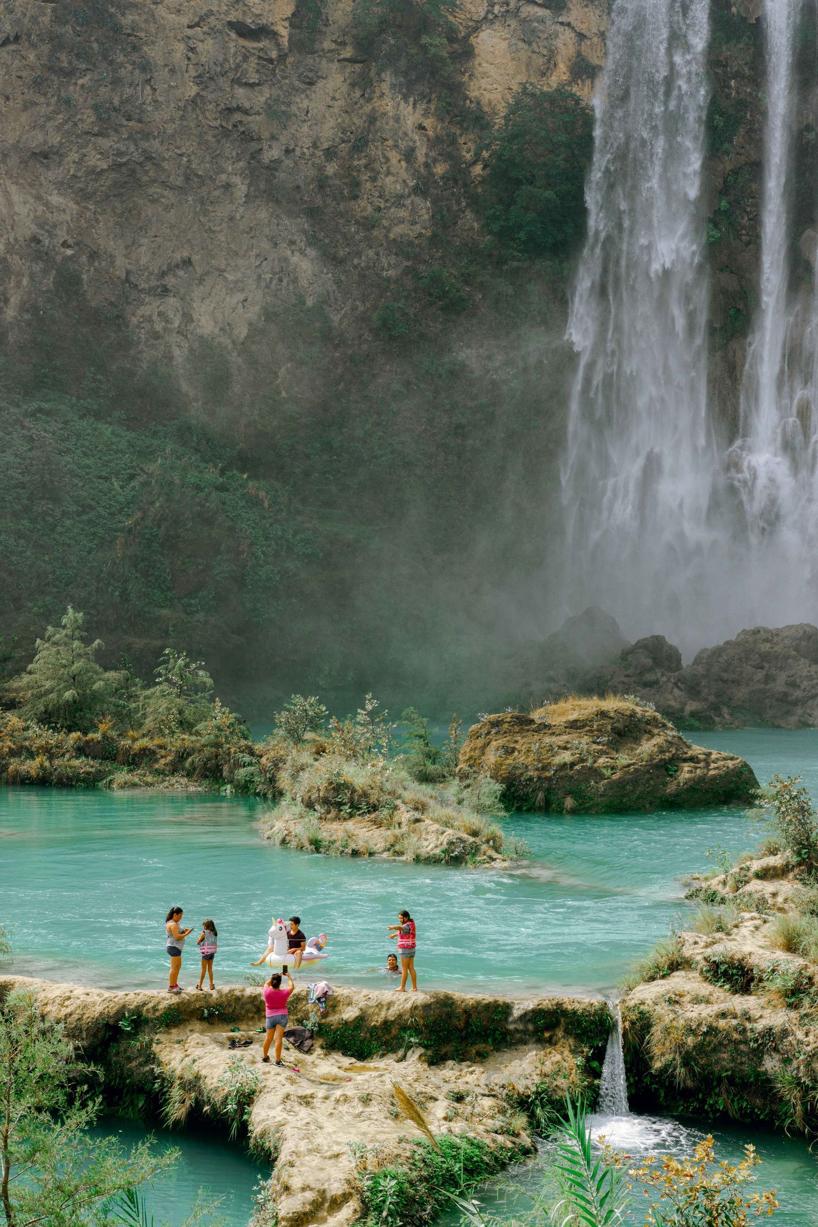 Tourists enjoying the turquoise waters and stunning waterfall in San Luis Potosí, Mexico.