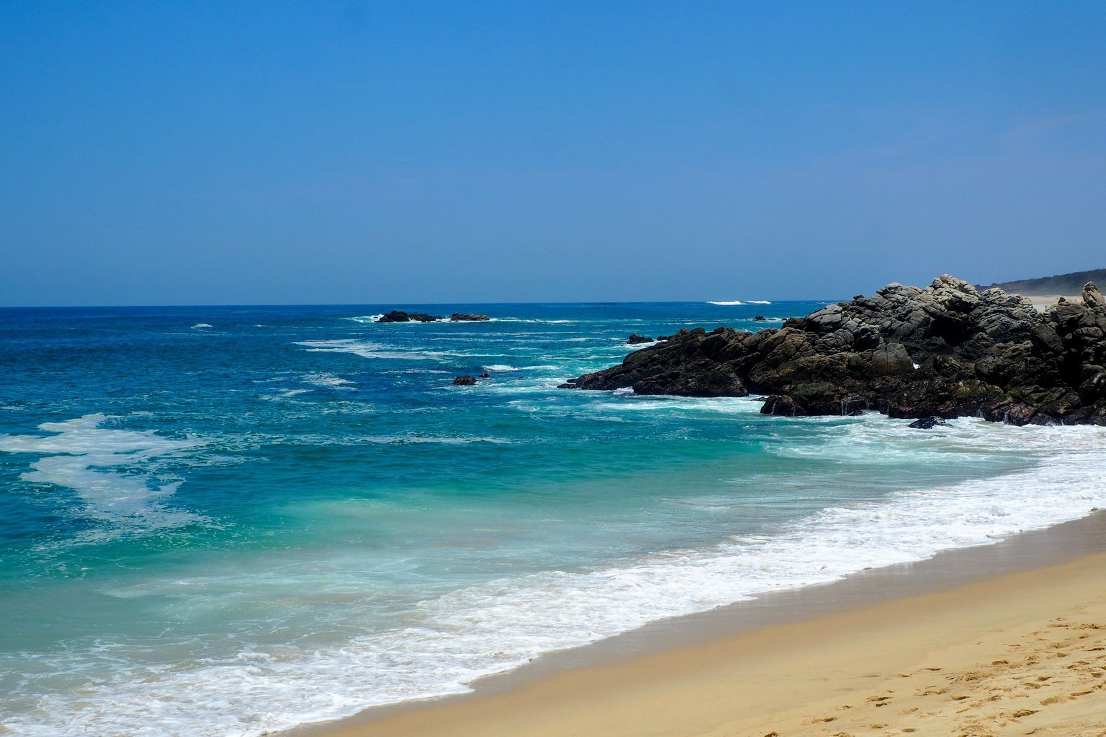 Tranquil view of Puerto Escondido's sandy beach with clear turquoise waters and rocky coastline.