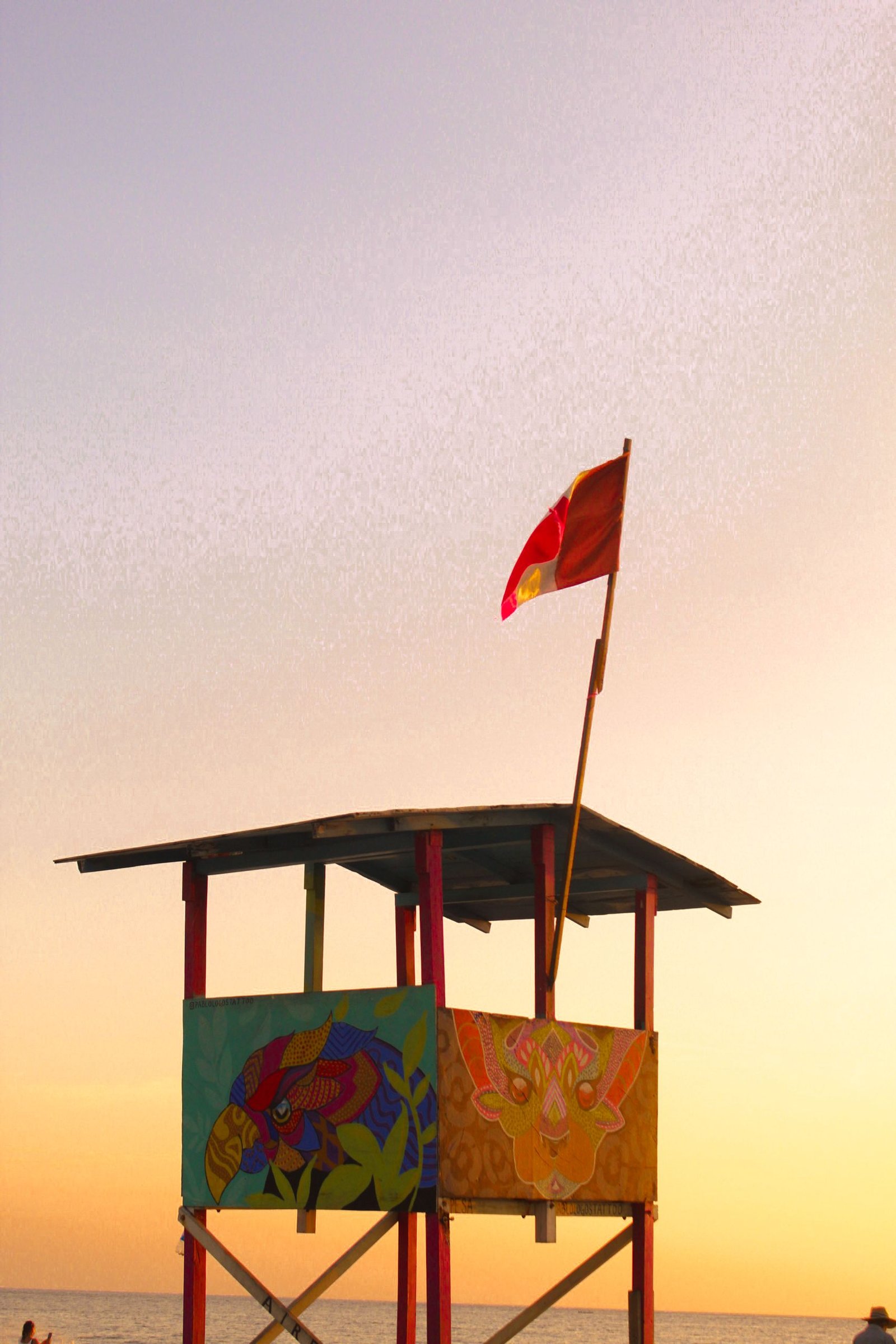 Vibrant lifeguard tower with flag against sunset sky on Puerto Escondido beach.