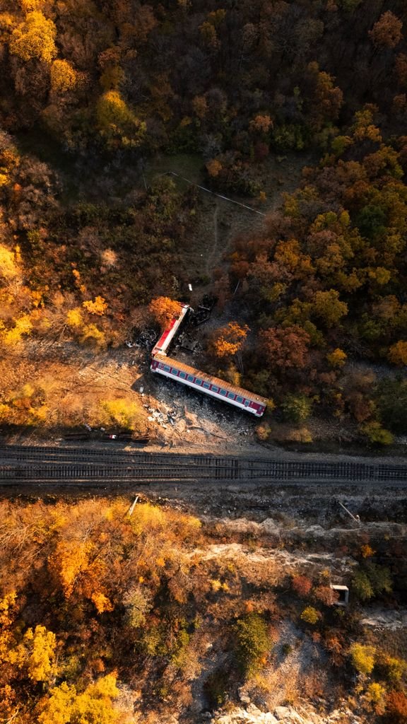 Drone capture of a train crash in Slovakia's vibrant autumn forest landscape, showcasing seasonal foliage.