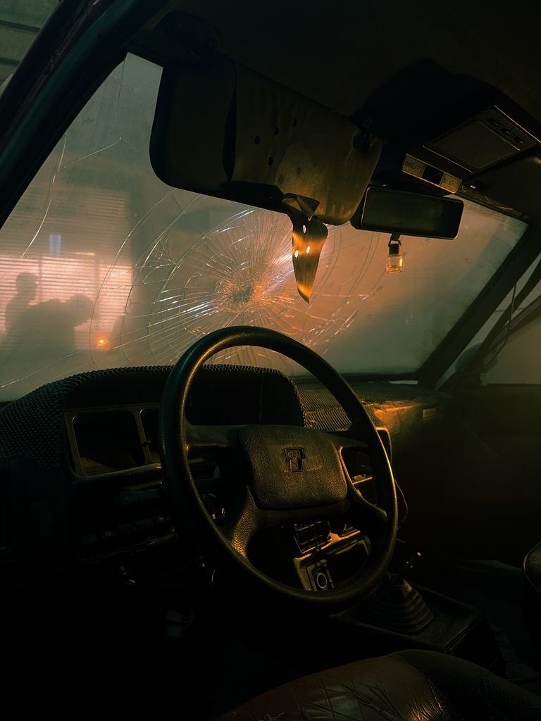 Moody car interior with shattered windshield, warm lighting and reflections at night.