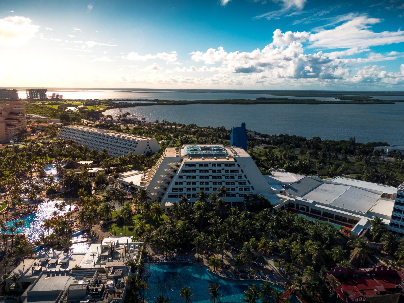 Stunning aerial view of a tropical beachfront resort in Cancun, Mexico, featuring lush palm trees and blue waters.