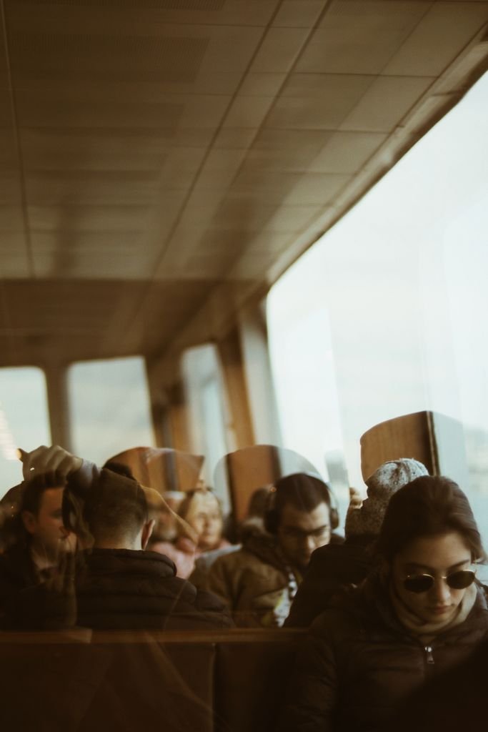 Through glass window view of passengers sitting on rows of bench while waiting for ferry in landing stage