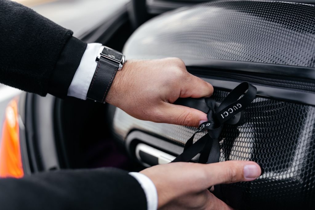 Close-up of hands unpacking an elegant suitcase from a car trunk, showcasing luxury fashion.