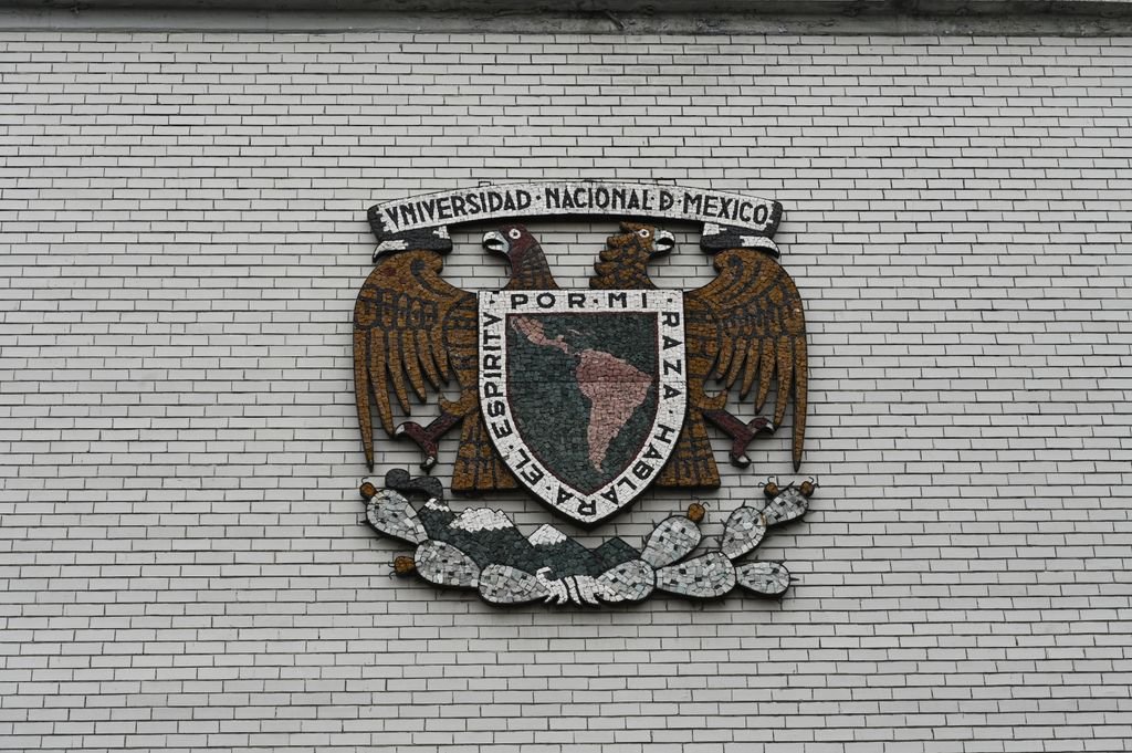 Close-up of the Universidad Nacional de Mexico crest on a white brick wall.