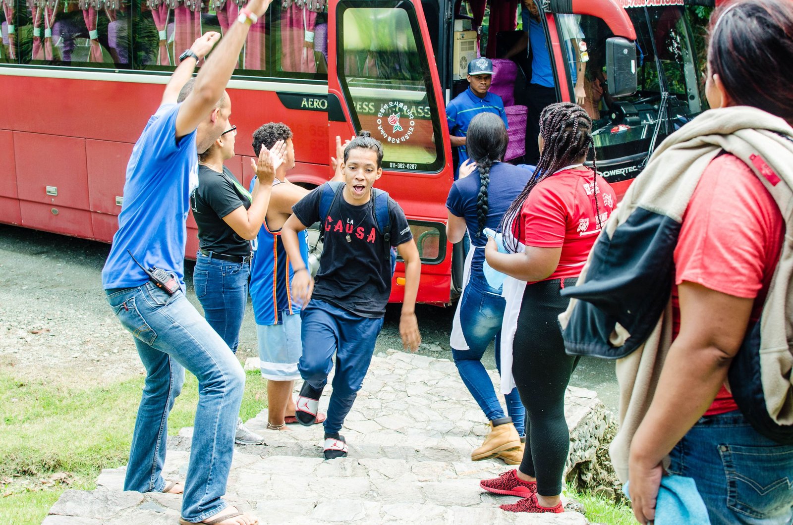Excited group of commuters cheer as they prepare to board a bus, capturing a moment of shared enthusiasm.