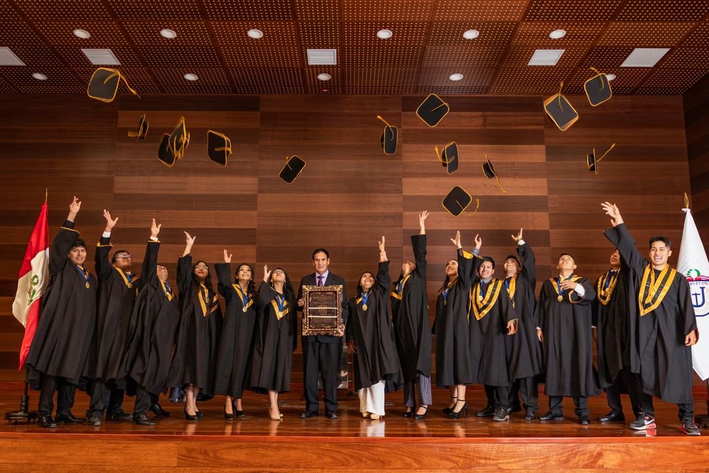 Graduates celebrating by tossing caps indoors in Tacna, Perú, marking their achievement with joy.