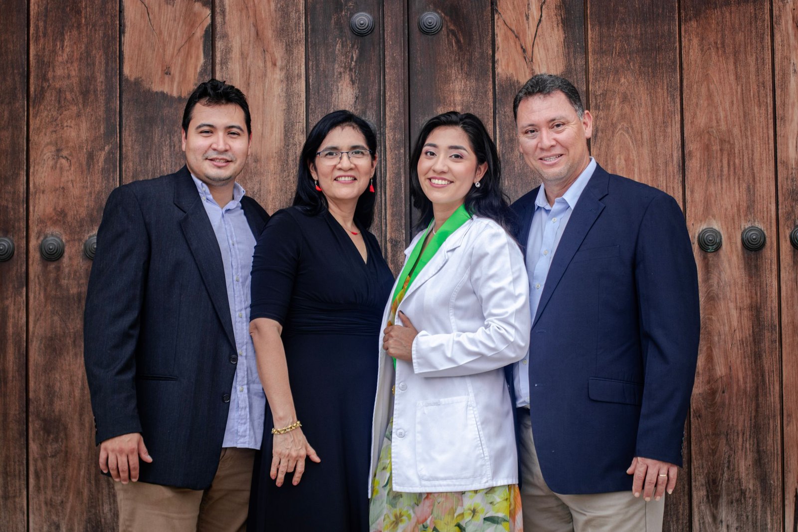 Group portrait of a smiling family in formal attire against wooden doors.