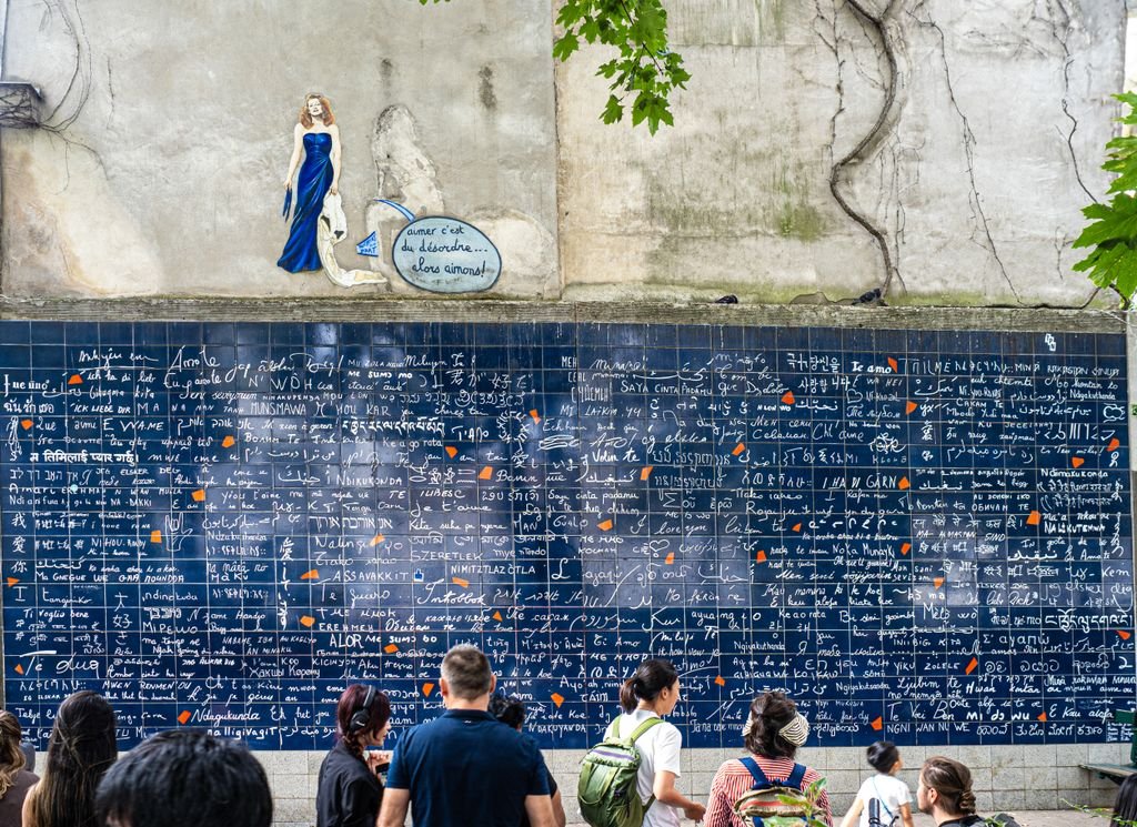 Visitors admire the iconic Wall of Love in Paris, featuring multiple languages and artistic elements.